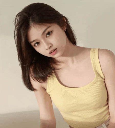 a young woman wearing a yellow tank top looks at the camera