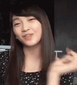 a woman with long hair is smiling and making a heart shape with her hands while wearing a black and white polka dot dress .
