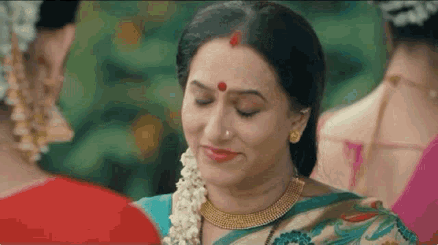 a woman in a saree with a red dot on her forehead is smiling .