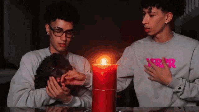 two young men are sitting at a table with a red candle and one of them is wearing a sweater with the letter r on it