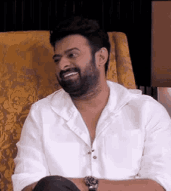 a man with a beard is sitting in a chair wearing a white shirt .