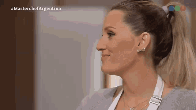 a woman in a ponytail is smiling in front of a masterchef argentina logo