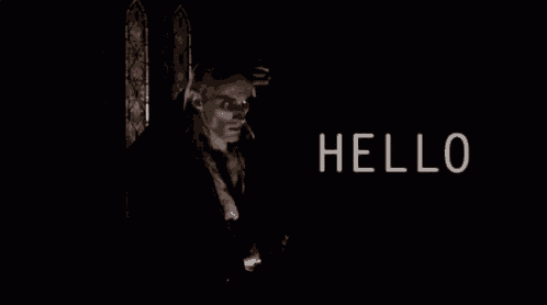 a man with long hair is standing in a dark room with the words `` hello '' written above him .