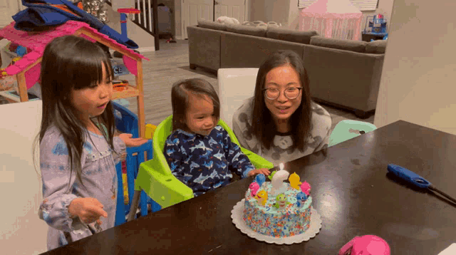 a woman sitting at a table with two children and a birthday cake