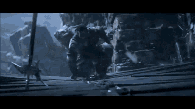 a man is kneeling down next to a sword in a dark cave .