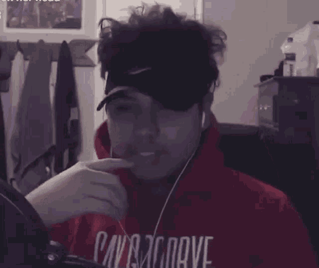 a man wearing a red hoodie and a hat is sitting in front of a computer screen .