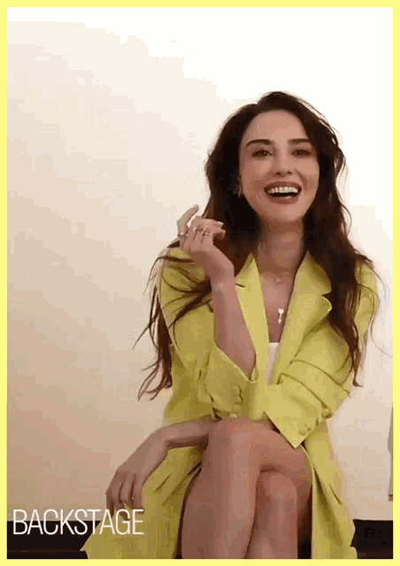 a woman in a yellow jacket is sitting on a chair and smiling