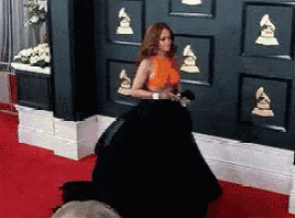 a woman is standing on a red carpet in front of a wall with awards on it .