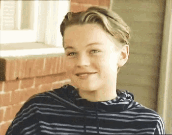 a young boy wearing a striped hoodie is standing in front of a brick wall .