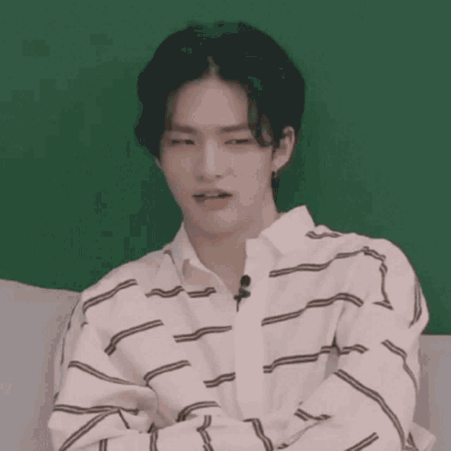 a young man in a striped shirt is sitting on a couch with his arms crossed and making a face .