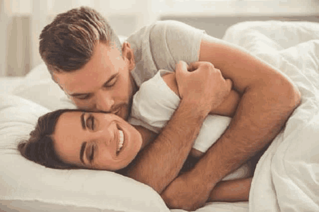 a man is kissing a woman on the forehead while laying in bed .