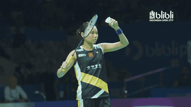 a woman holding a badminton racket with the word blibli on the bottom right