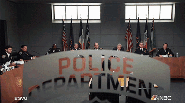 a group of police officers sit at a table in front of a sign that says " police department "