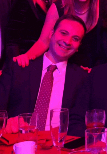 a man in a suit and tie sitting at a table with wine glasses