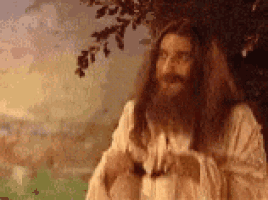 jesus with long hair and a beard is standing in front of a tree .