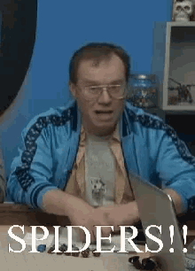 a man in a blue jacket is sitting at a table with a laptop and the words spiders on the screen