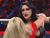 two women are wrestling in a ring and one is wearing a red shirt .