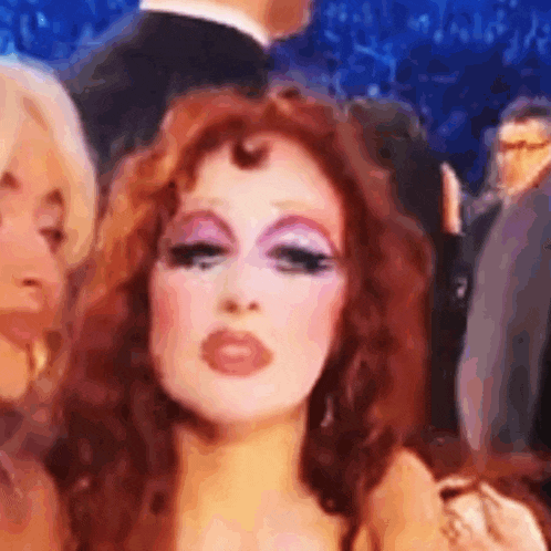 a woman with red hair and pink makeup is standing in a crowd .