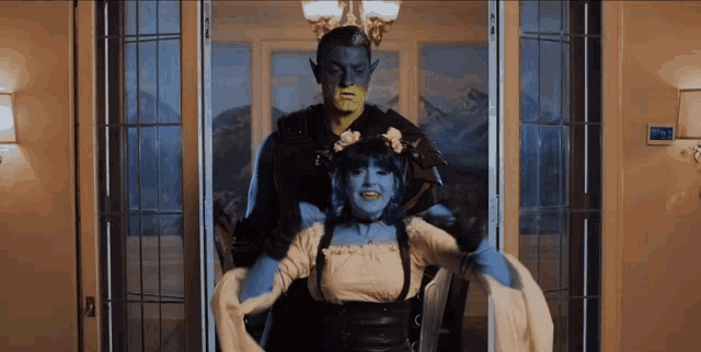 a man with green paint on his face is holding a woman in a blue costume