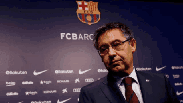 a man in a suit and tie stands in front of a fc barc sign