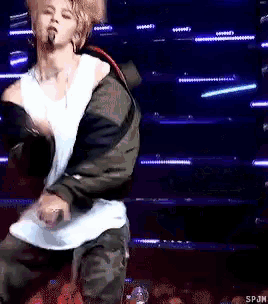 a man in a white tank top is dancing on a stage with a microphone in his mouth .