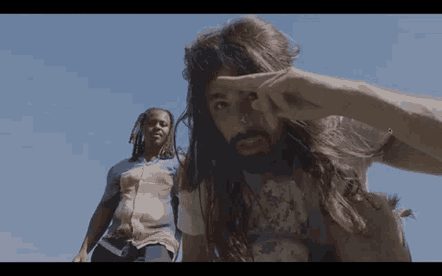 a man with long hair and a beard is standing next to another man with dreadlocks
