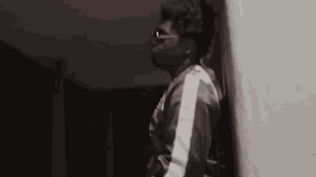 a man is leaning against a wall in a dark room wearing sunglasses .