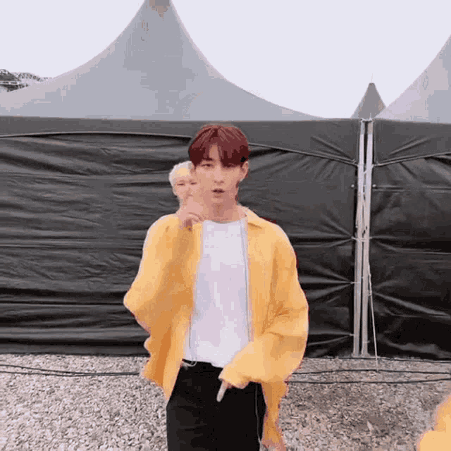 a young man wearing a yellow jacket and a white shirt is pointing at something