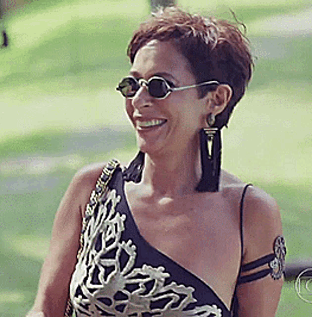 a woman wearing sunglasses and a one shoulder dress is smiling