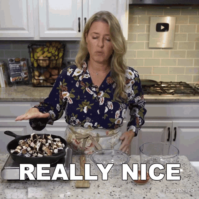 a woman in a floral shirt is standing in a kitchen and says really nice