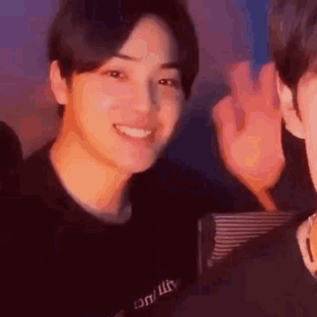 a close up of a person smiling and waving at the camera while another person looks on .