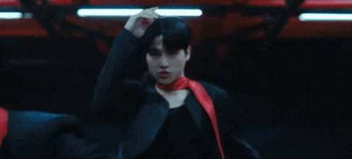 a man wearing a black shirt and a red scarf around his neck is dancing in a dark room .