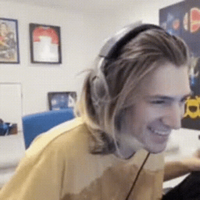 a man wearing headphones and a yellow hoodie is smiling while sitting in front of a computer .