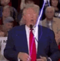 a man in a suit and tie is speaking into a microphone while a lightning bolt is coming out of his mouth .