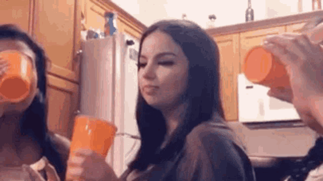 a woman is drinking from an orange cup in a kitchen while two other women drink from orange cups .