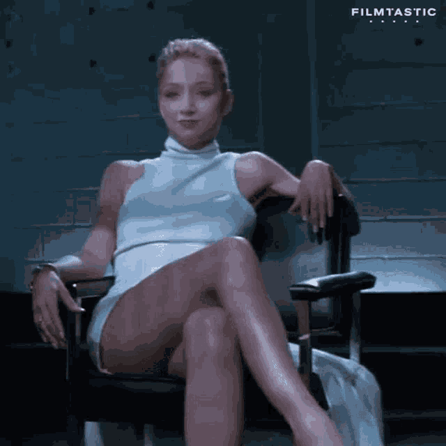 a woman in a white dress is sitting in a chair with her legs crossed and her hands on her knees .