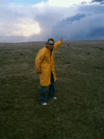 a man in a yellow raincoat and sunglasses stands in a grassy field
