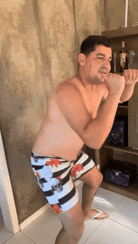 a shirtless man in floral shorts is squatting
