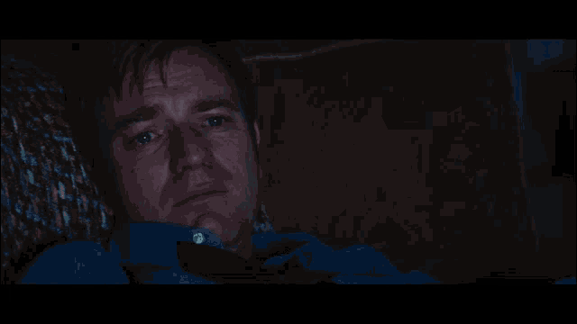 a man in a blue shirt and tie is laying down in a dark room