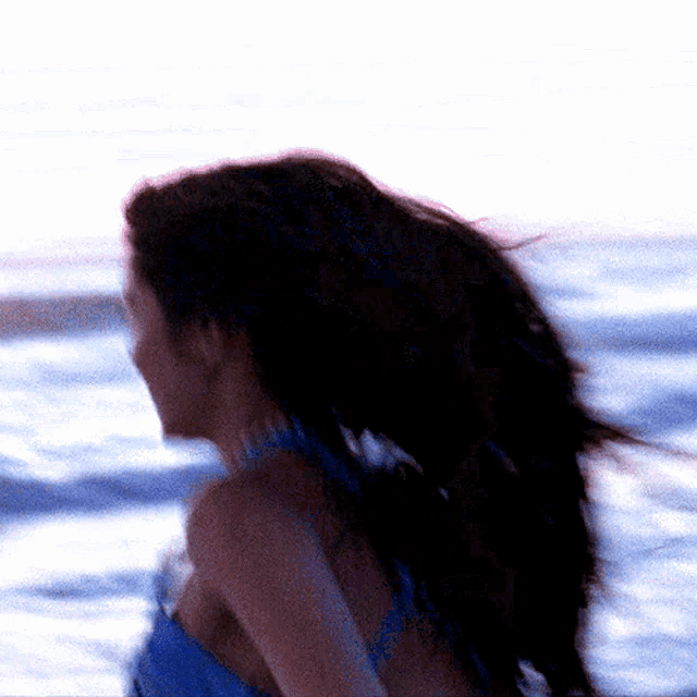 a woman in a blue top is standing in front of a body of water