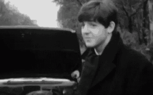 a black and white photo of a young man standing next to a car .