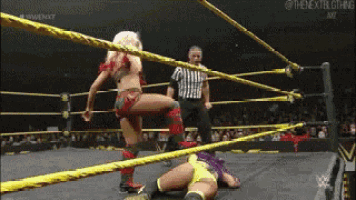 a female wrestler is kicking another wrestler in the ring while a referee watches