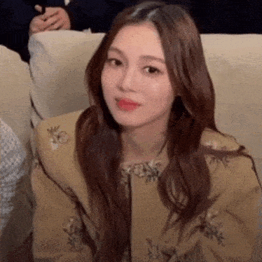 a woman with long hair is sitting on a couch looking at the camera .