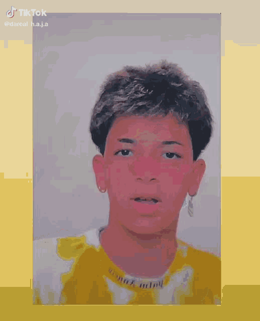 a young man wearing a yellow and white tie dye shirt and earrings is looking at the camera .