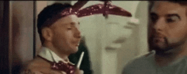 two men are standing next to each other in a room . one of the men is wearing a bandana .