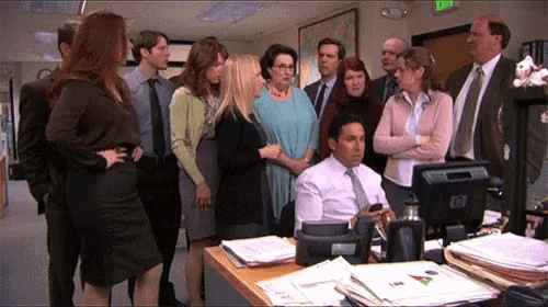 a group of people standing around a man sitting at a desk with an hp computer monitor