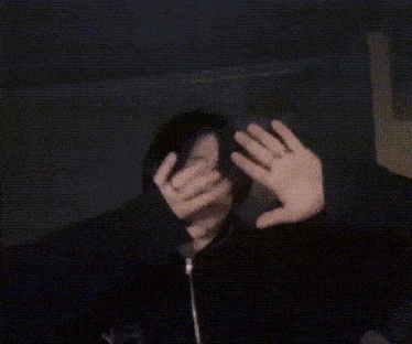 a person covering their face with their hands while wearing a black jacket with the letter u on it