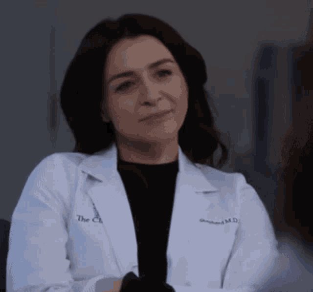 a woman wearing a white lab coat and a black shirt is sitting with her arms crossed .