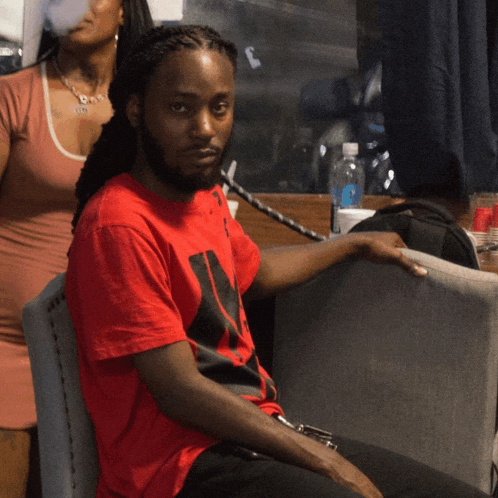 a man in a red shirt sits in a chair with a woman behind him