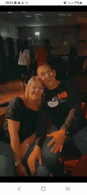 a man and a woman are posing for a picture and the man is wearing a bab shirt